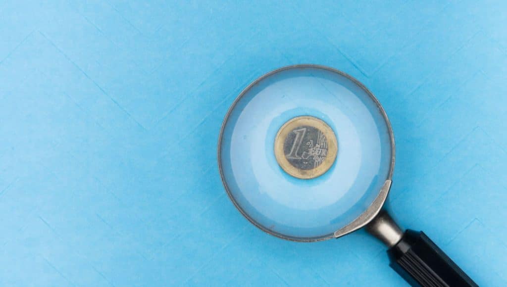 Una lente d'ingrandimento su sfondo blu che migliora la visibilità di una moneta in euro.